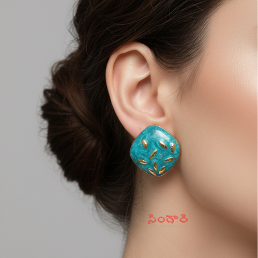 Turquoise earrings with gold accents worn by a model on a gray background